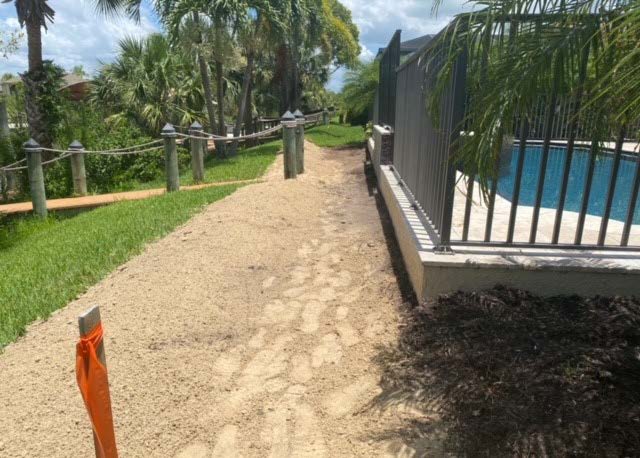 Photo of a backyard with a walkway, grass, dirt, edge of a pool deck and a survey stake